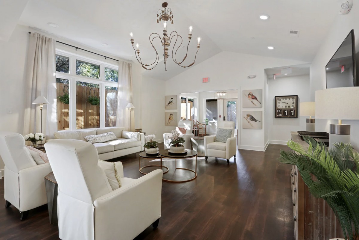 A modern and elegant living room with white furniture, a chandelier, and hardwood floors.