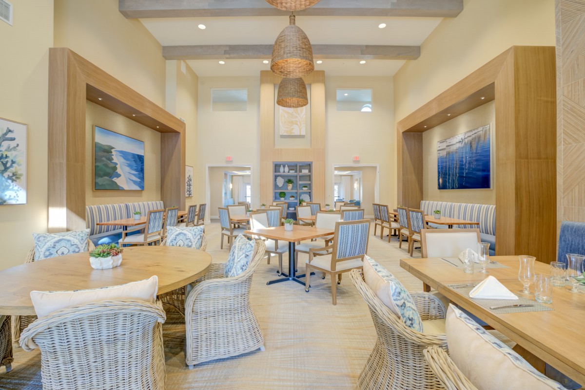 A spacious dining area with wicker chairs, round tables, and artwork on the walls.