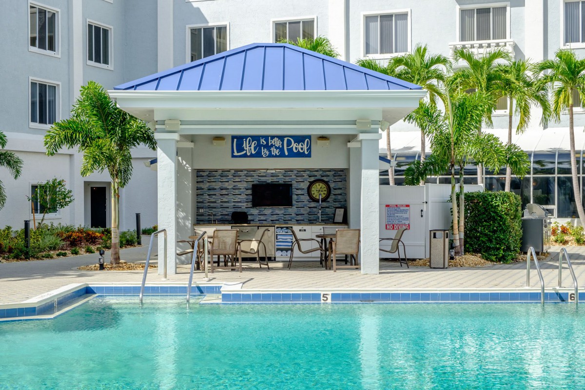 An inviting outdoor pool with a bar and seating area, surrounded by palm trees at a hotel.