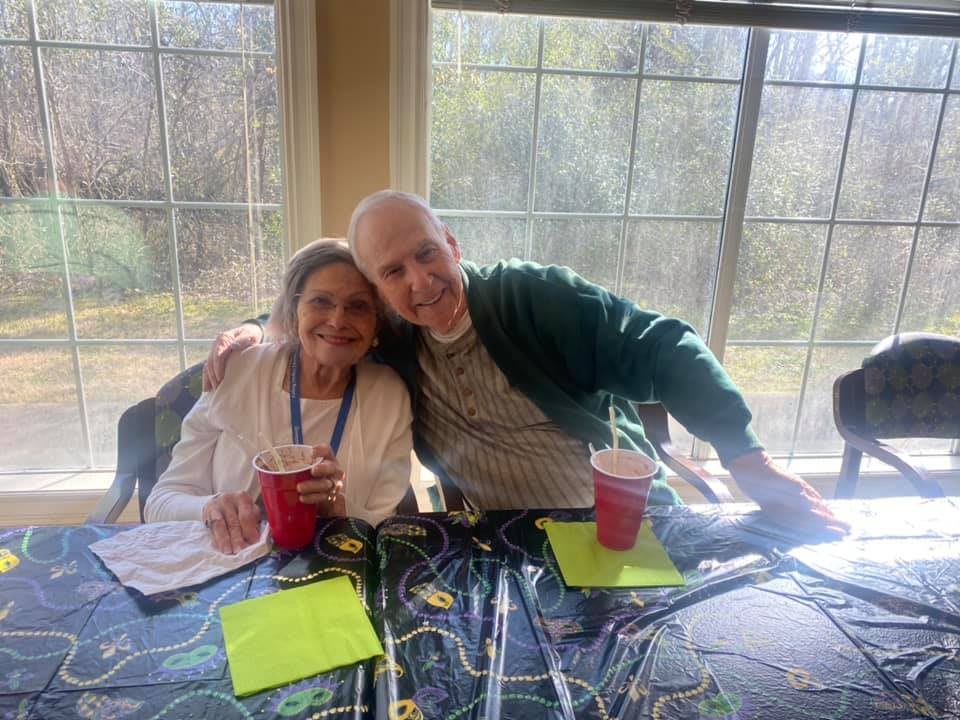 A couple sitting together at a table indoors, holding drinks and enjoying each other's company.