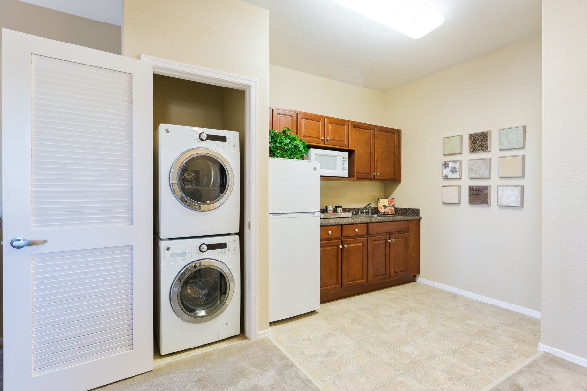 A modern laundry room with a stacked washer and dryer, alongside a kitchen area featuring wooden cabinets and a refrigerator.