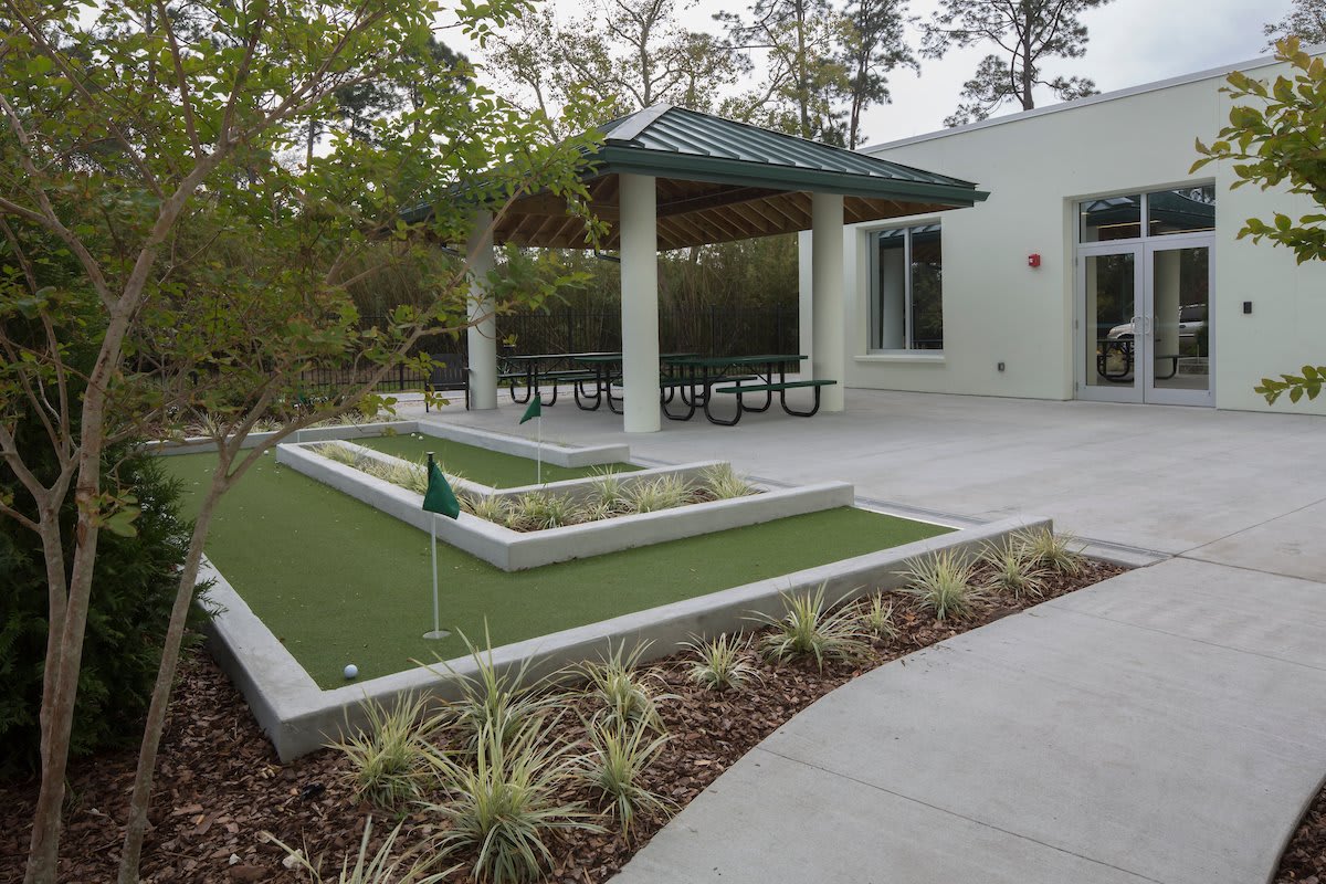 An outdoor mini-golf area with artificial turf, sheltered seating, and surrounding greenery.
