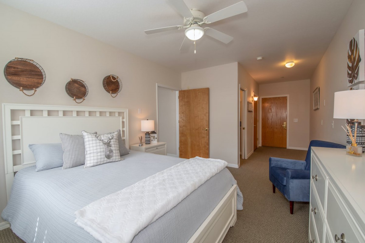 A cozy and minimalist bedroom with a large bed, ceiling fan, and soft lighting.