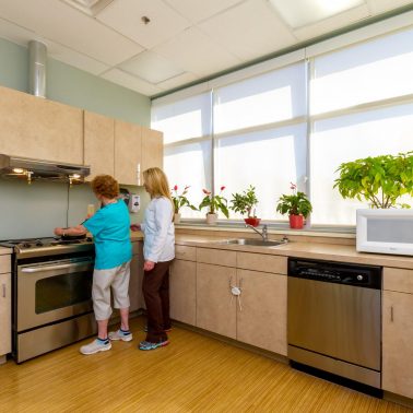 Two individuals are engaged in cooking activities in a bright, modern kitchen filled with plants.