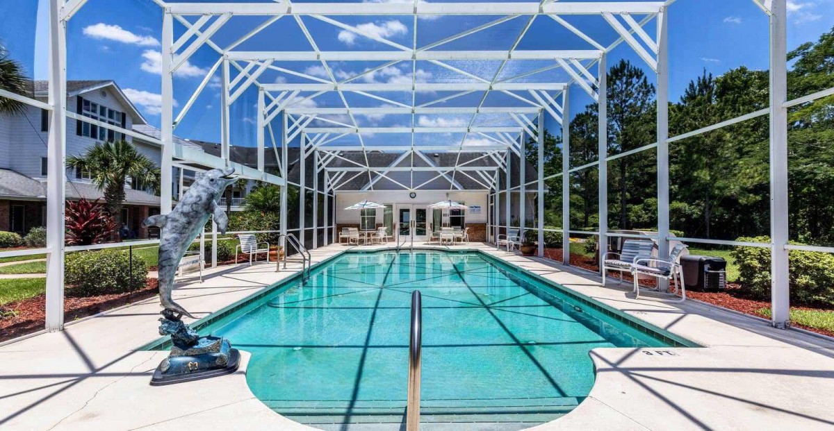 A spacious indoor swimming pool with a glass ceiling and clear blue sky visible above.