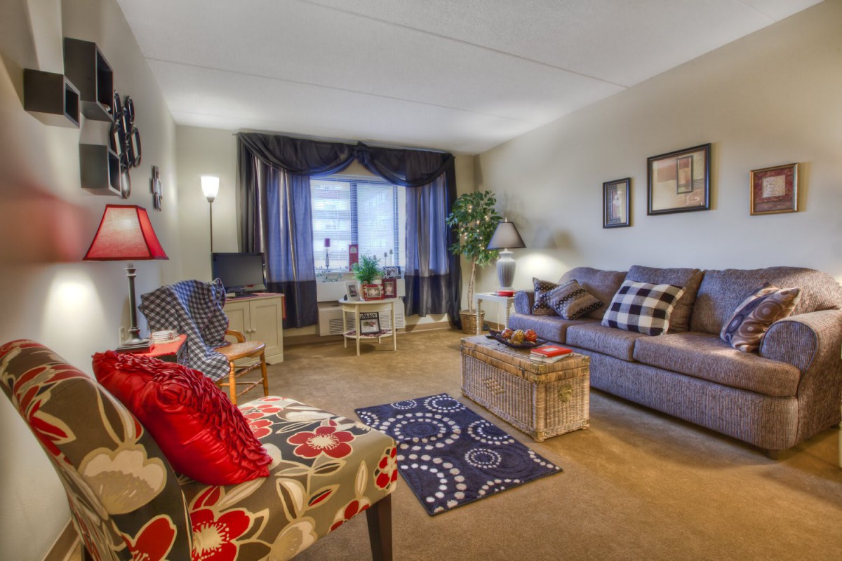 A cozy living room featuring comfortable seating, colorful decor, and a large window bringing in natural light.