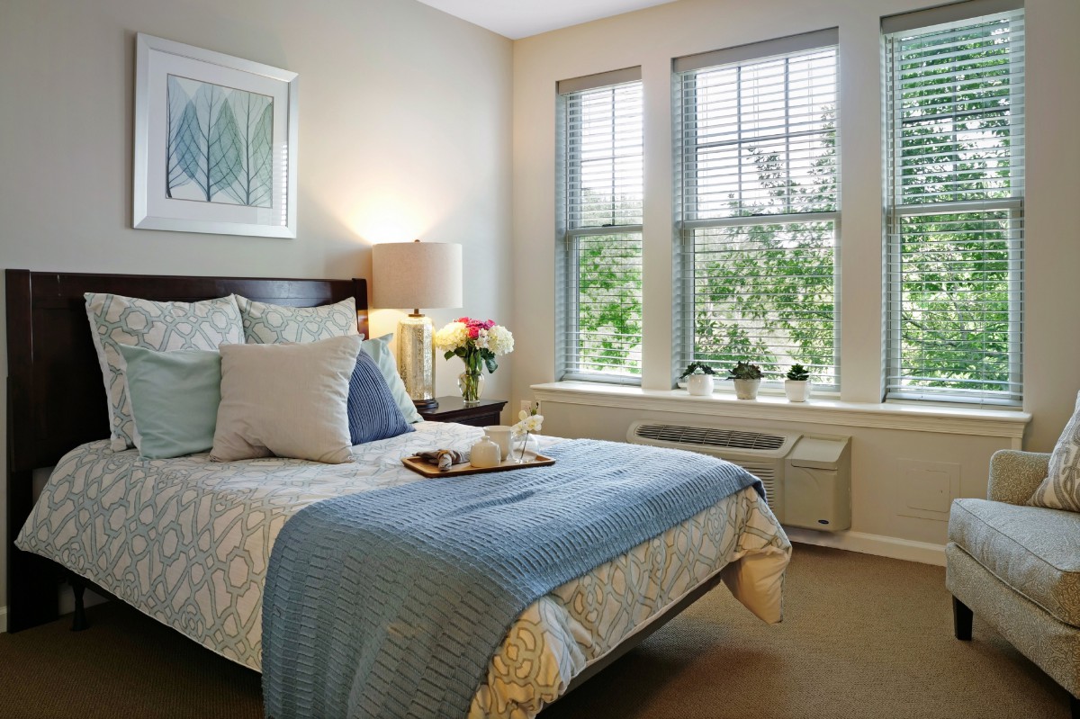 A cozy bedroom with a neatly made bed, large windows, and inviting decor.