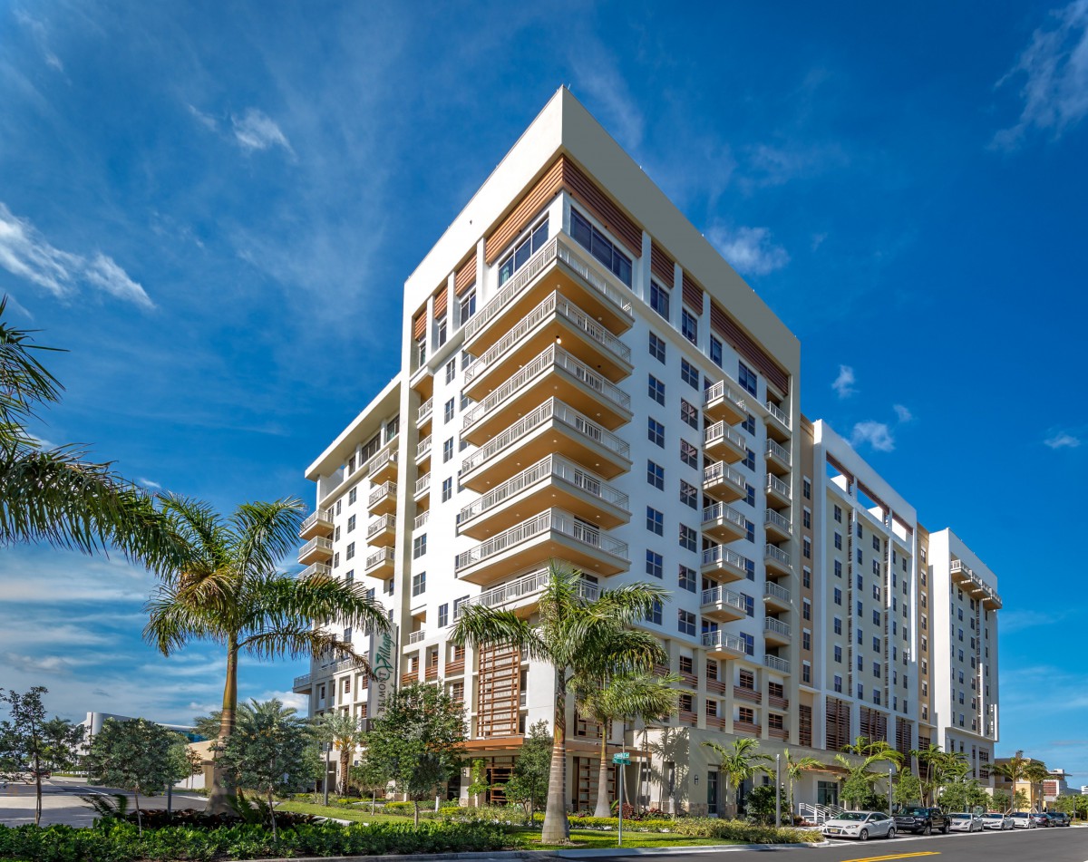 A modern high-rise apartment building surrounded by palm trees under a clear blue sky.
