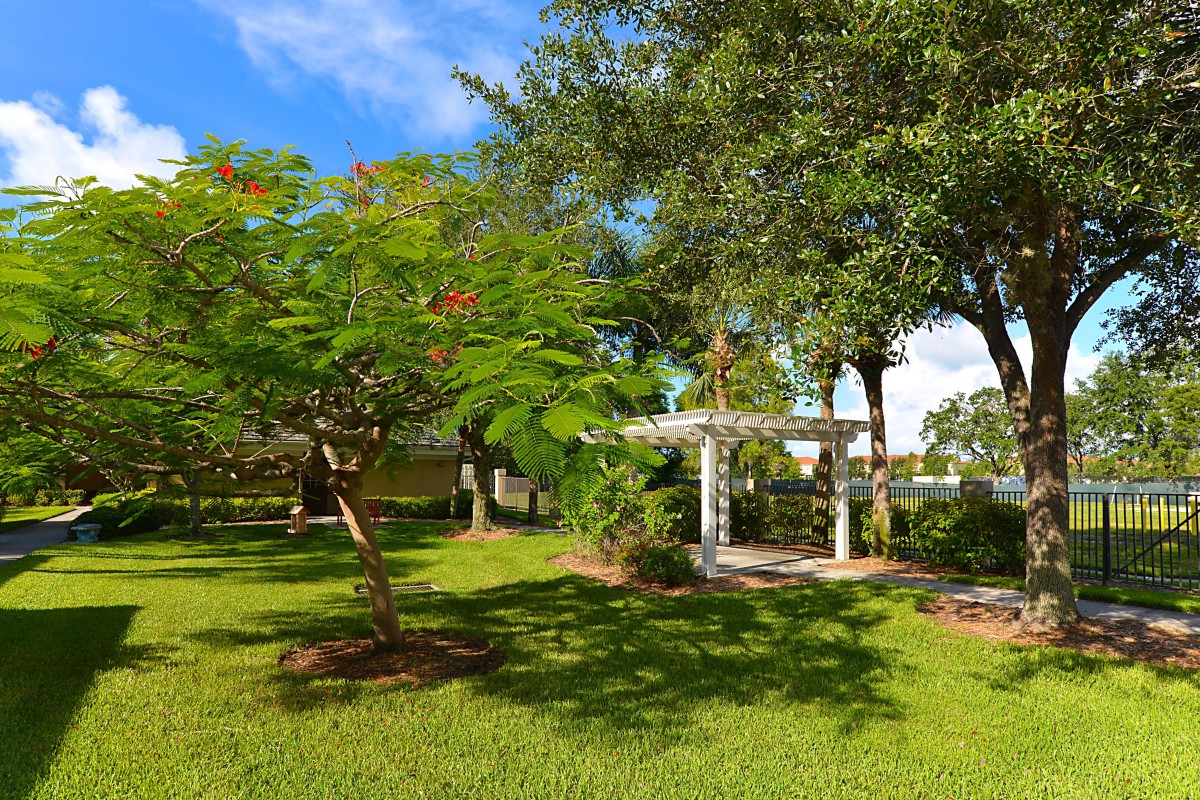 A serene garden with lush greenery and a white pergola under a clear blue sky.