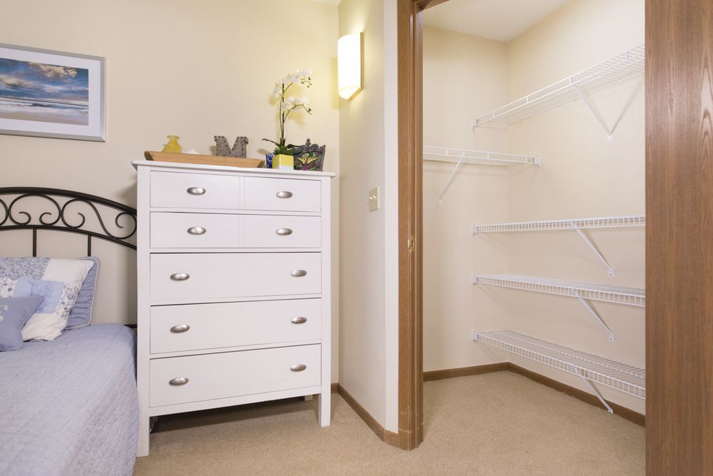 A tidy bedroom space featuring a white dresser and an open walk-in closet.