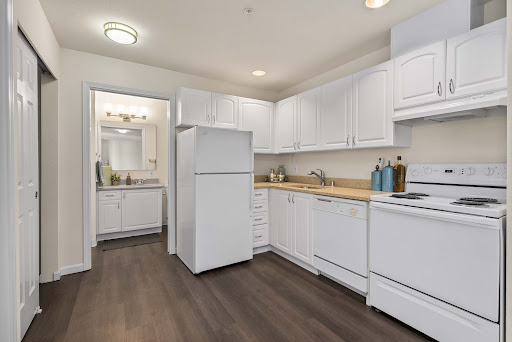 A modern kitchen featuring white cabinetry and appliances, complemented by warm wood flooring.
