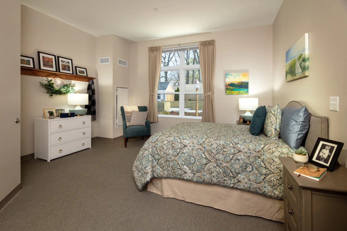 A cozy bedroom with a large bed, desk, and window letting in natural light.