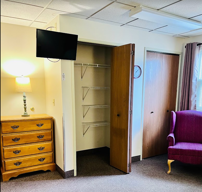 A cozy room with a TV, closet, lamp, dresser, and upholstered chair.