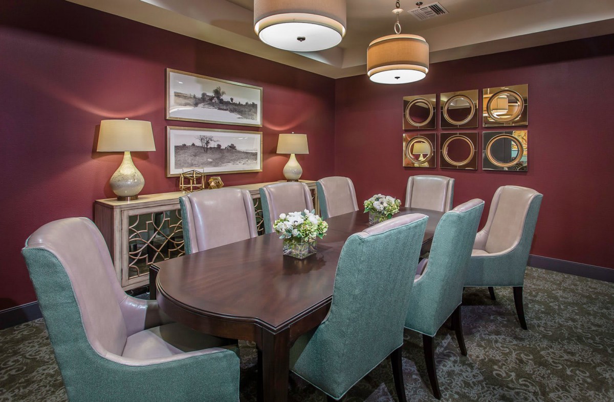 A modern dining room with a large wooden table, surrounded by upholstered chairs and decorated with ambient lighting and wall art.