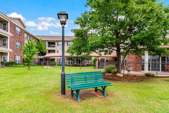 A green bench next to a lamp post on a grassy area with trees and a building in the background.