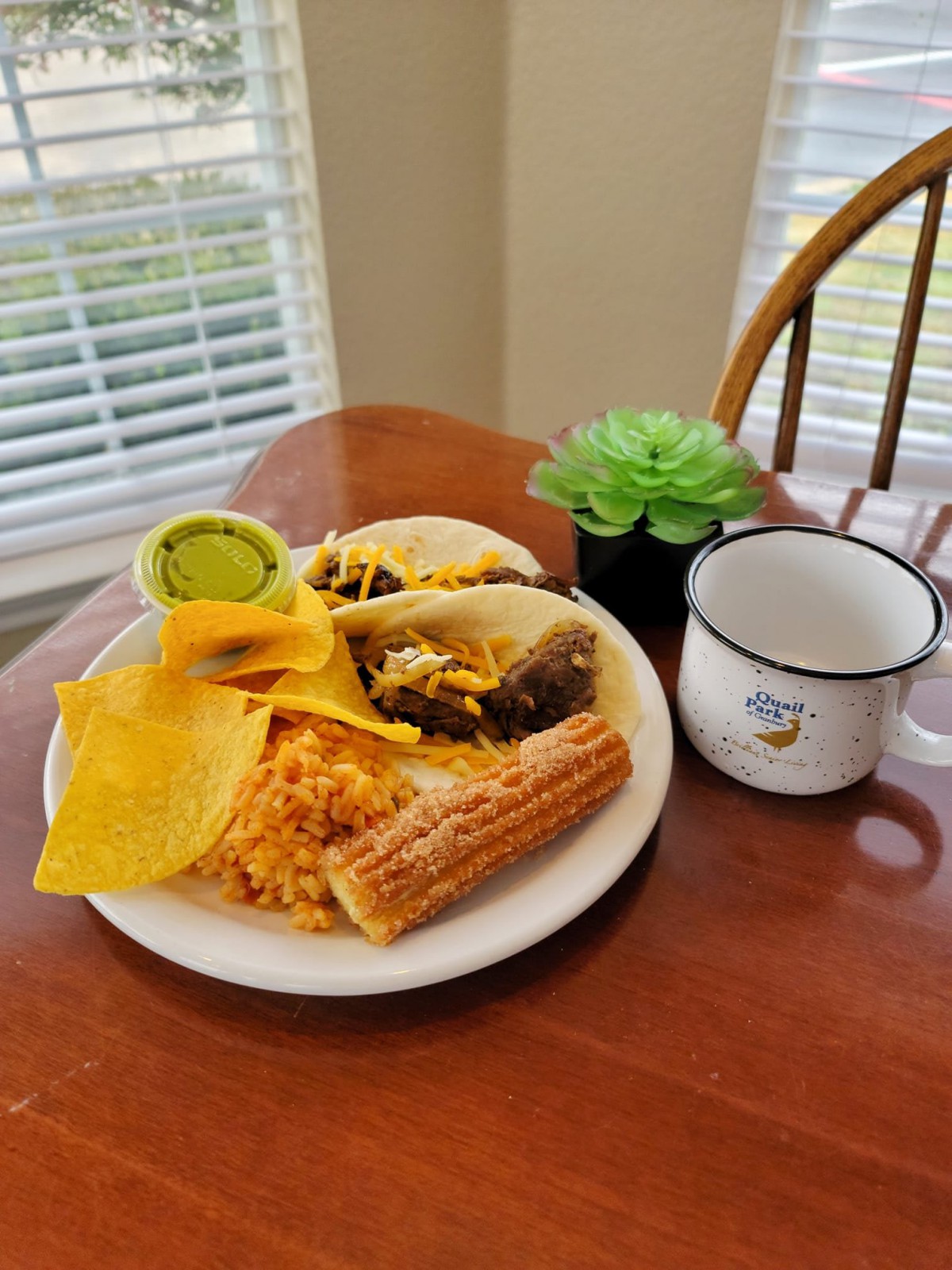 A delicious Mexican breakfast featuring tacos, rice, a churro, and guacamole on a plate.