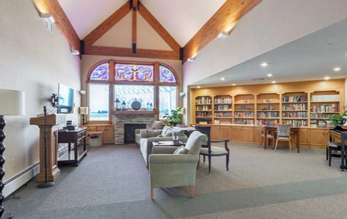 A cozy library with comfortable seating, bookshelves, a fireplace, and a stained glass window.