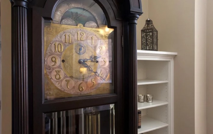 An antique grandfather clock stands next to white shelves in a cozy interior setting.