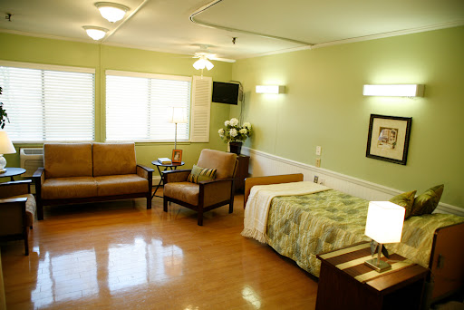 A well-lit and spacious hospital room featuring comfortable seating and a neatly made bed.