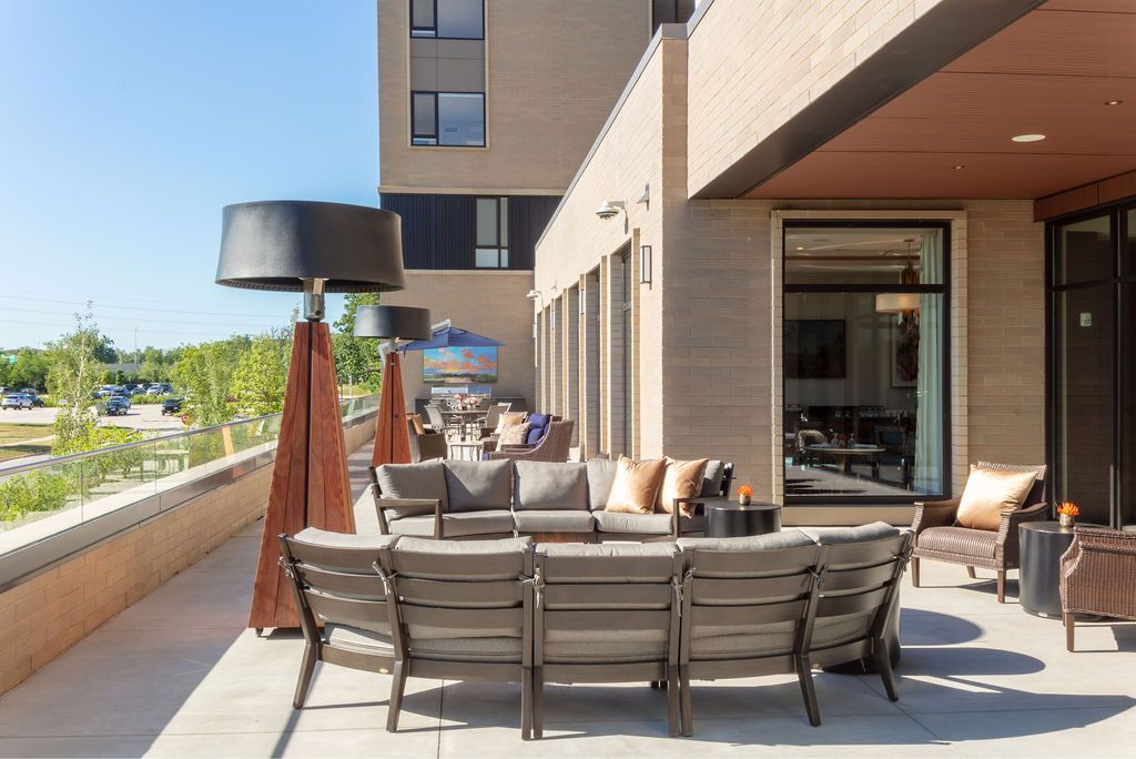 A modern outdoor patio area featuring comfortable seating and heater lamps, set against the backdrop of a building exterior.