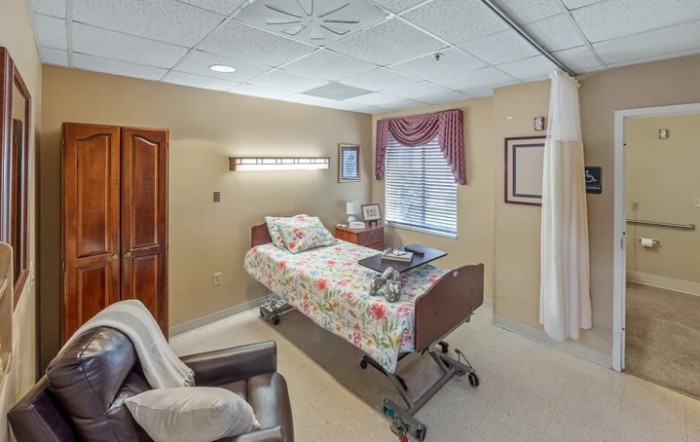 A well-appointed hospital room featuring a patient bed, comfortable seating, and a large window with curtains.
