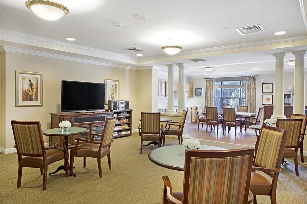 A cozy and well-lit living area with tables, chairs, and a large television.