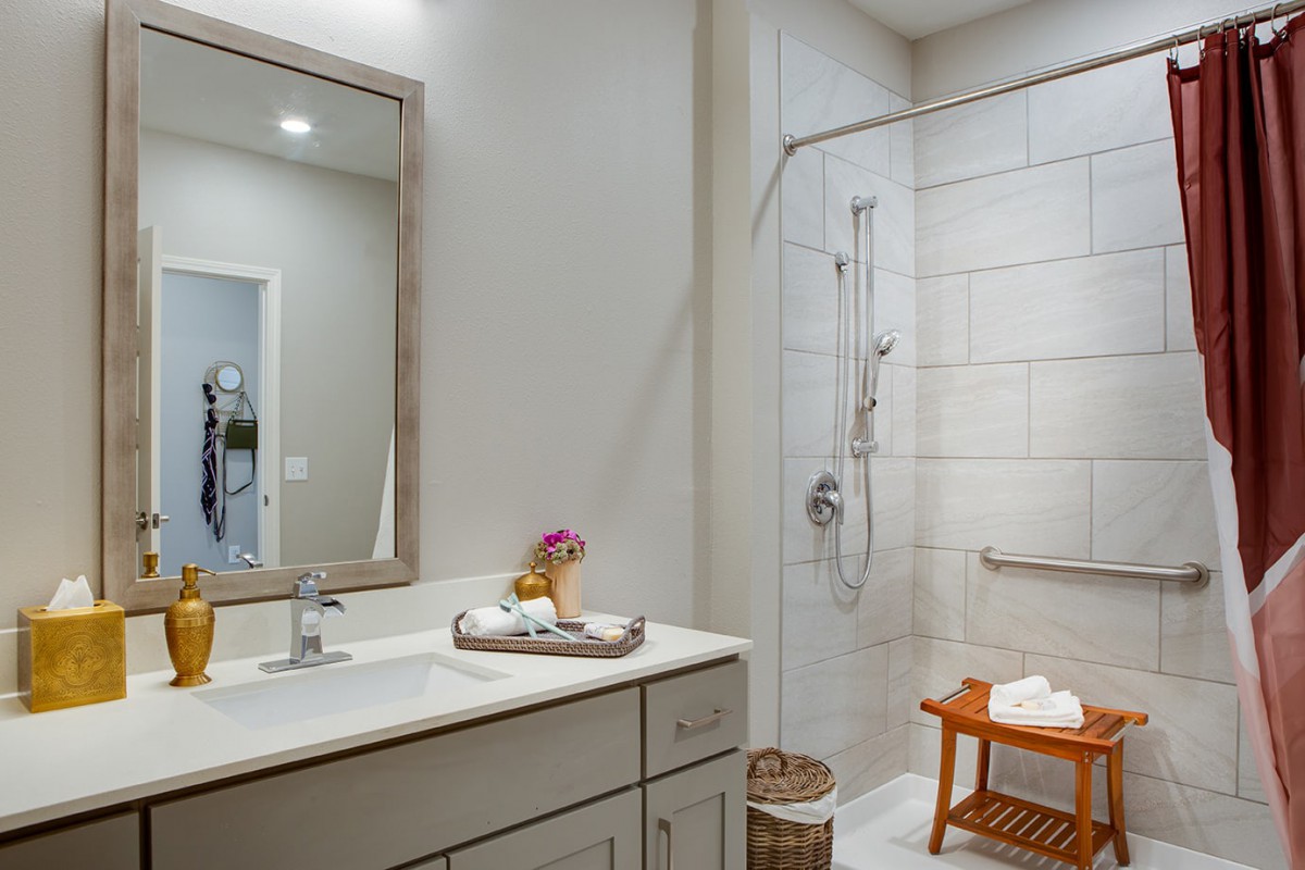 A modern bathroom with a large mirror, sink, and walk-in shower.