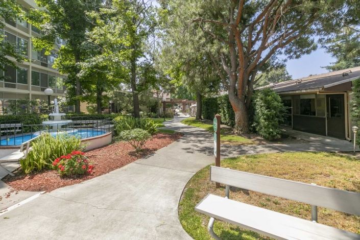A peaceful garden with a winding pathway, benches, and lush greenery.