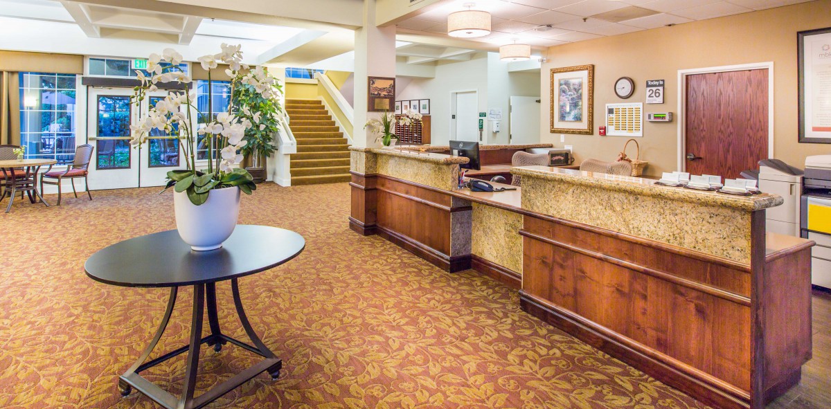 A hotel lobby with a reception desk and a staircase in the background.