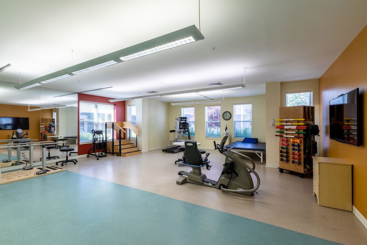 A clean and spacious fitness center equipped with various exercise machines and rehabilitation equipment.