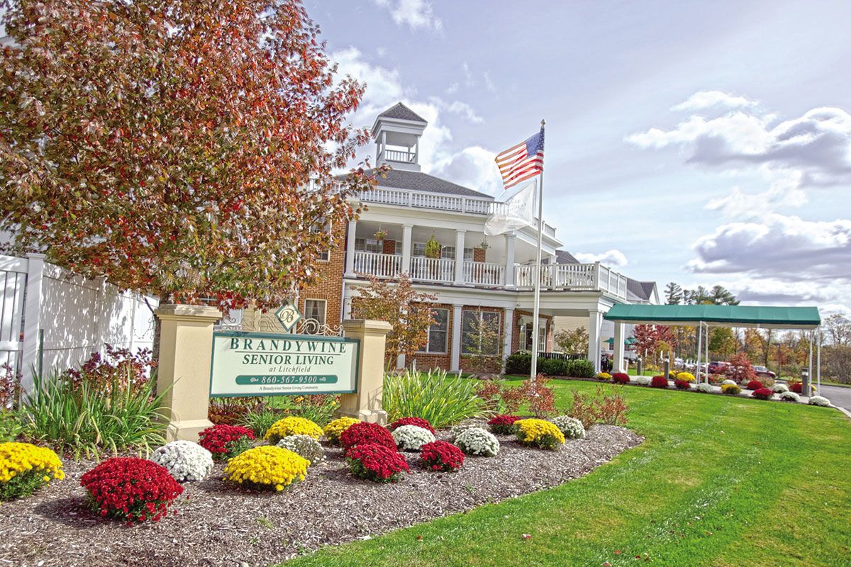 A scenic view of a building with an American flag, surrounded by colorful flowers and autumn trees.