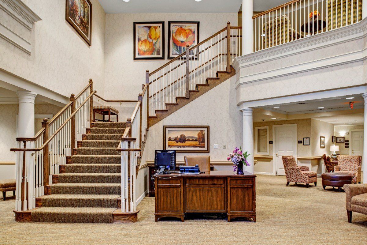 A spacious lobby with a reception desk and a grand staircase, featuring elegant artwork on the walls.
