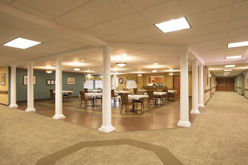 An empty dining room with tables, chairs, and columns under warm lighting.