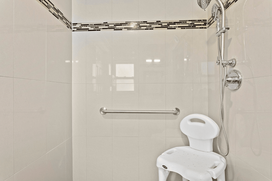 A bathroom with a shower featuring a chair and grab bar for accessibility.