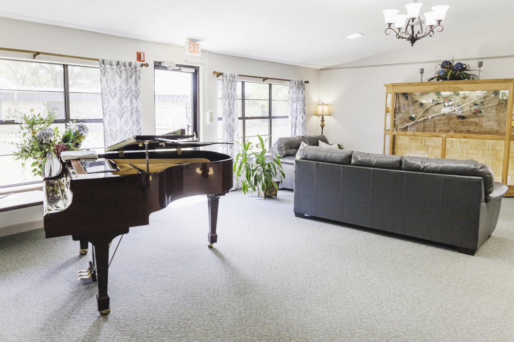 A bright and spacious living room featuring a grand piano, comfortable sofa, and large windows allowing natural light to fill the space.