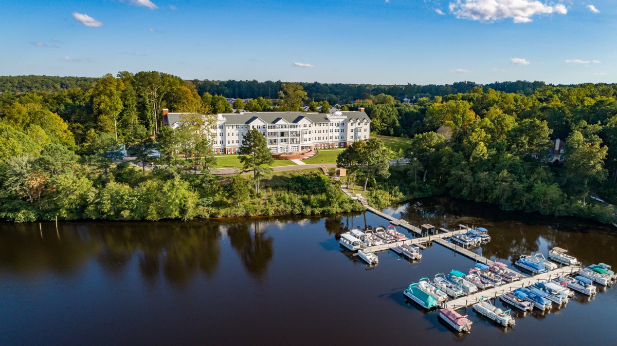 Aerial view of a lakeside building with docks and boats surrounded by trees.