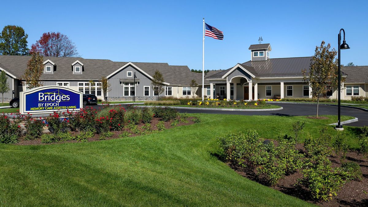 A scenic view of a building complex with well-maintained gardens and an American flag waving under a clear blue sky.