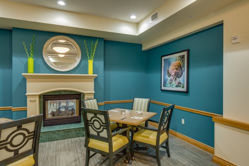 A cozy dining area with a table for four, featuring a blue accent wall, a fireplace, and decorative artwork.
