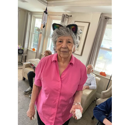 An elderly woman in a pink shirt wearing playful cat ears, enjoying her time indoors.