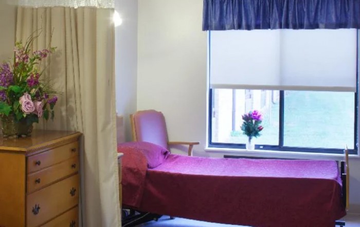 A hospital room with a single bed, dresser, and window adorned with flowers.