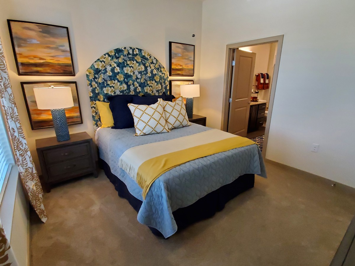 A cozy bedroom featuring a stylish bed with patterned headboard, flanked by two lamps and artwork on the walls.