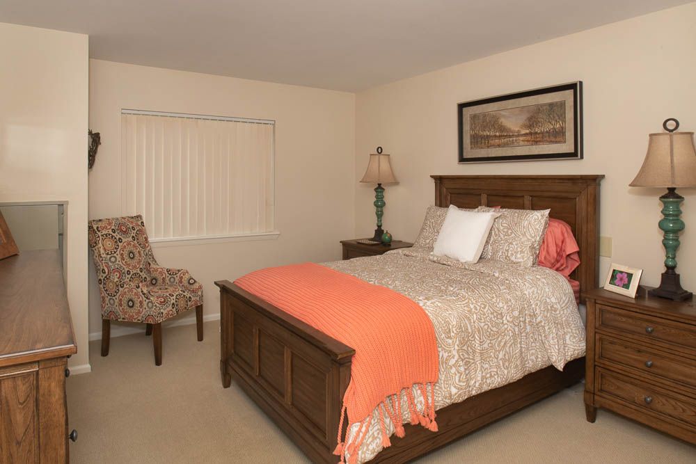 A cozy bedroom featuring a wooden bed with patterned bedding, a decorative lamp, and a patterned chair.