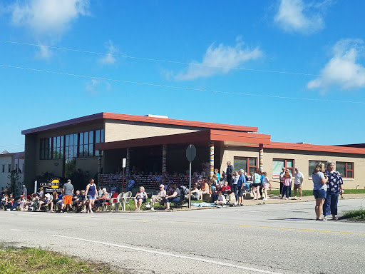 A group of people waiting outside a school building on a sunny day.