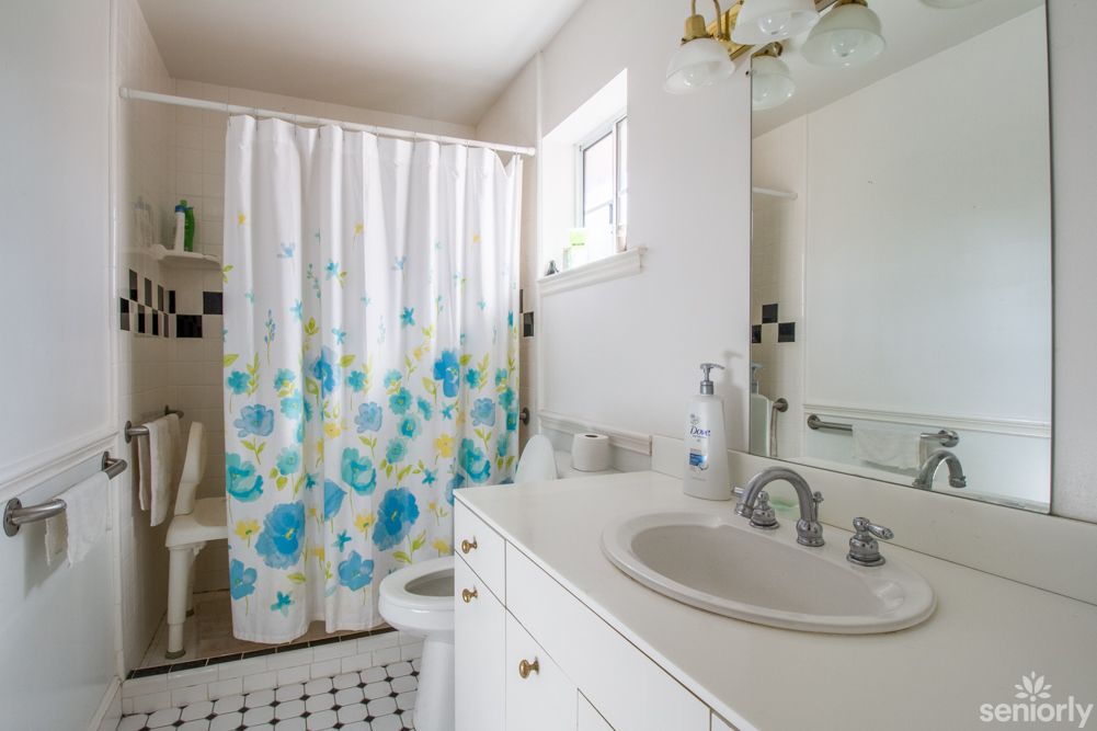 A bright bathroom with a floral shower curtain and white cabinetry.