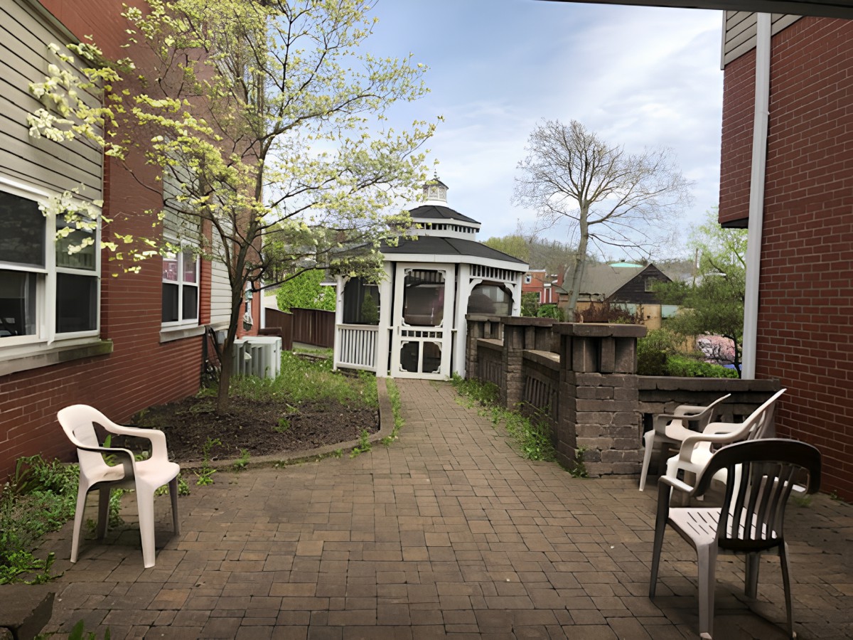 A serene garden with a gazebo and surrounding greenery, featuring a brick pathway and chairs.