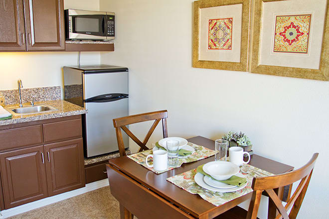 A cozy kitchen with a dining table set for two, featuring a microwave and refrigerator.