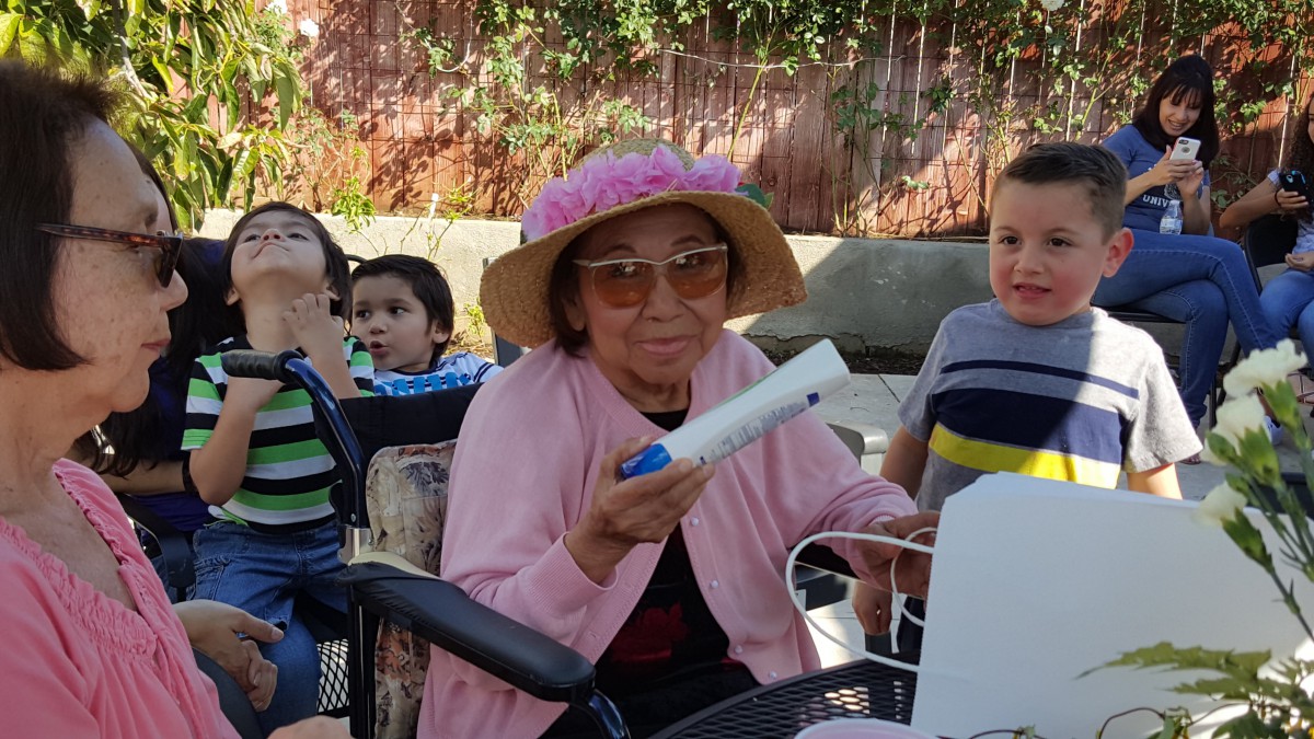 An elderly woman in a pink hat and sunglasses enjoys time with children during an outdoor gathering.