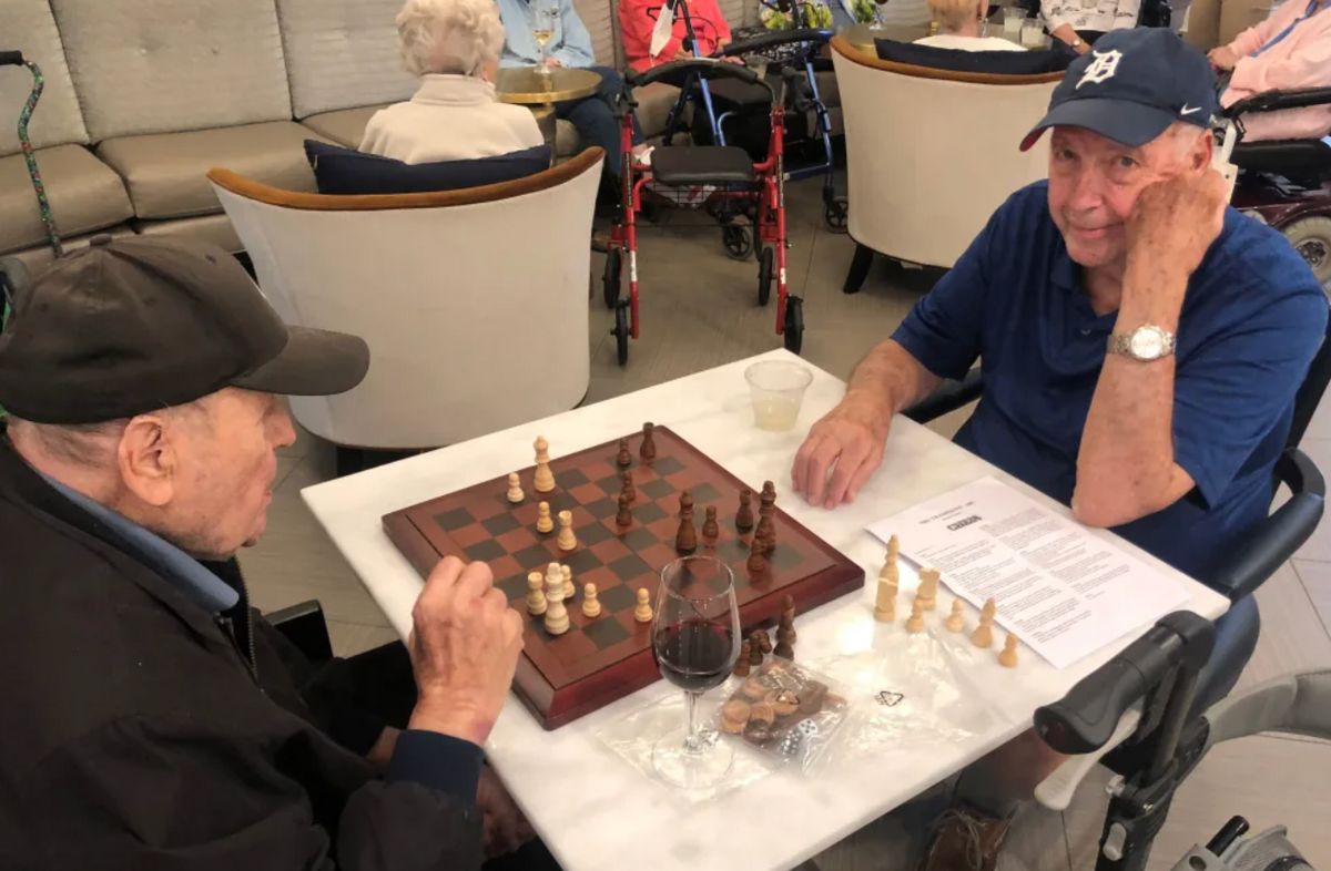 Two seniors engaged in a game of chess at a cafe.