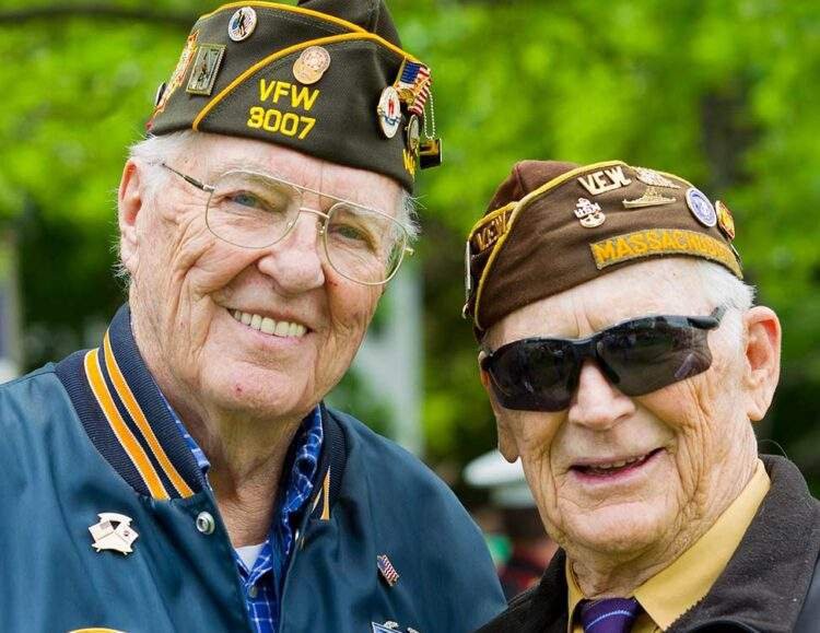 Two elderly veterans wearing VFW uniforms and hats, standing outdoors.