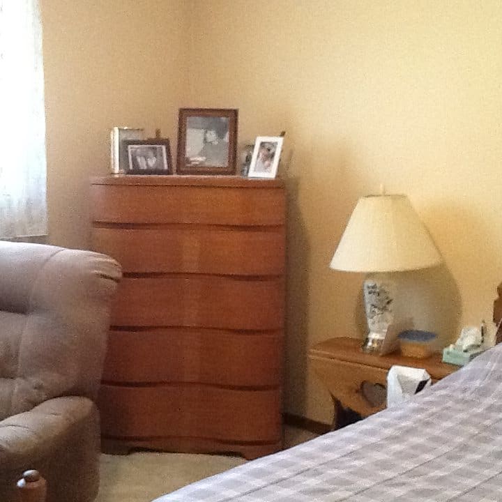 A cozy bedroom corner with a dresser and a lamp beside a comfortable chair.